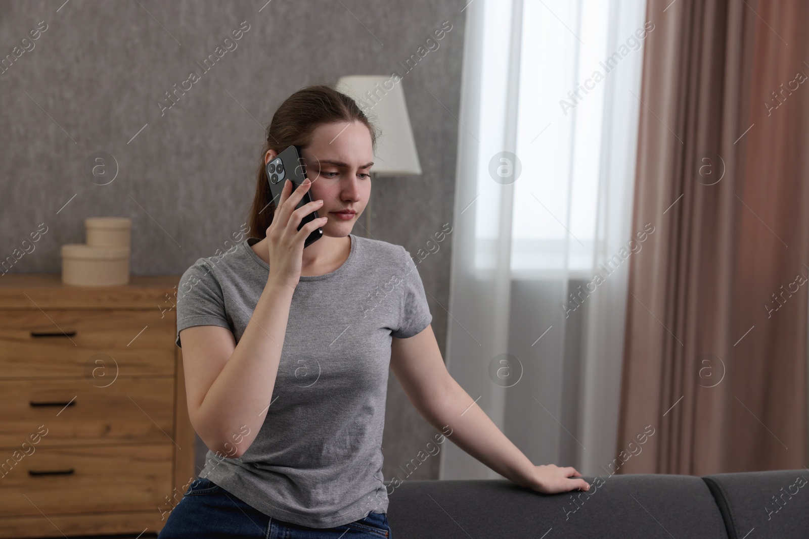 Photo of Depressed woman calling hotline for mental health help on sofa at home. Space for text