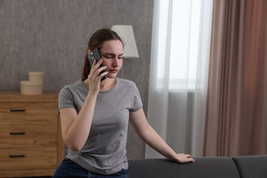 Photo of Depressed woman calling hotline for mental health help on sofa at home. Space for text