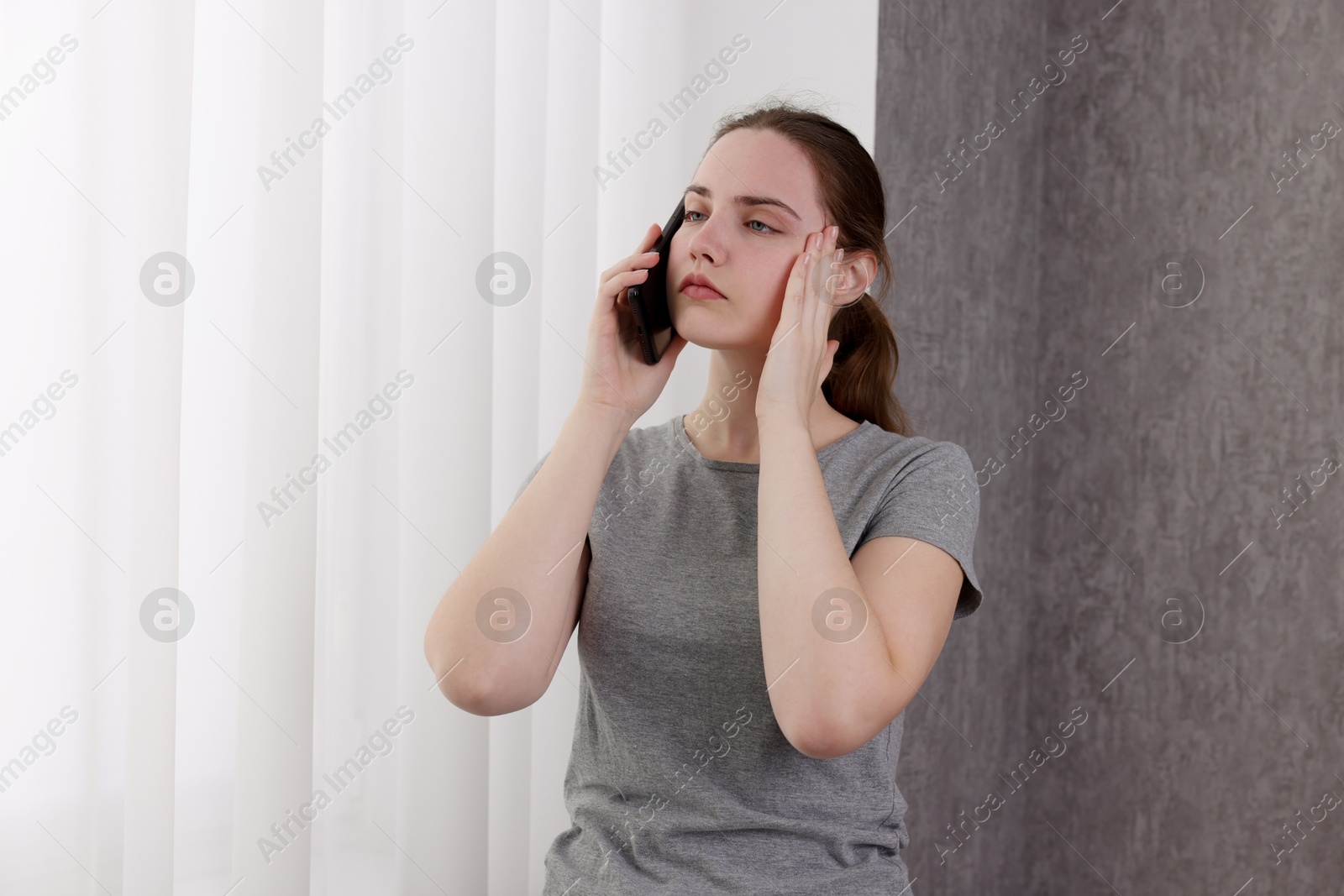 Photo of Stressed woman calling hotline for mental health help near window at home. Space for text