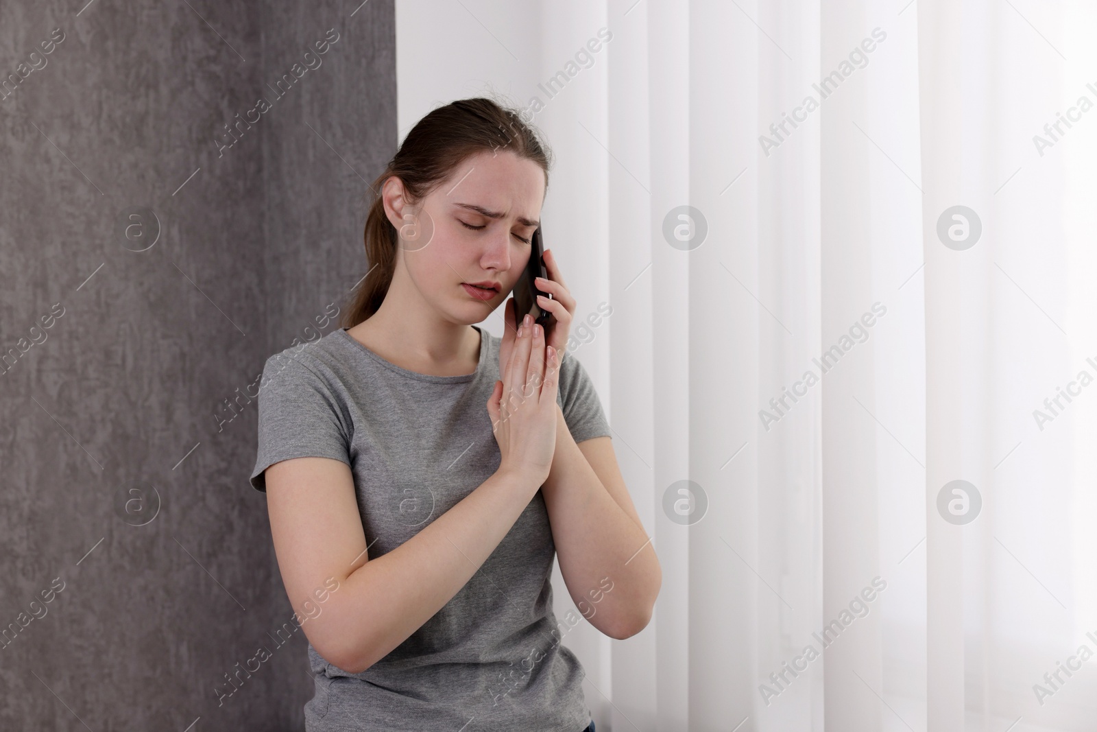 Photo of Stressed woman calling hotline for mental health help near window at home. Space for text