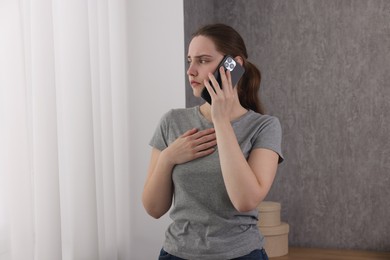 Photo of Stressed woman calling hotline for mental health help near window at home. Space for text