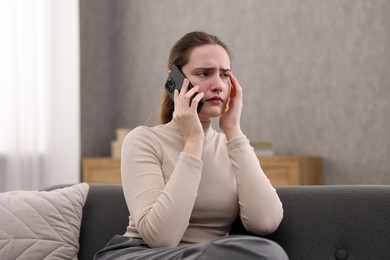 Photo of Depressed woman calling hotline for mental health help on sofa at home