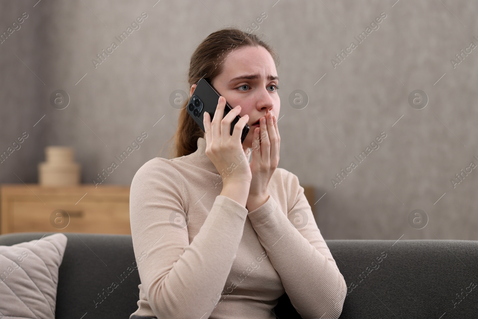 Photo of Depressed woman calling hotline for mental health help on sofa at home