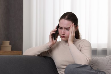 Photo of Depressed woman calling hotline for mental health help on sofa at home