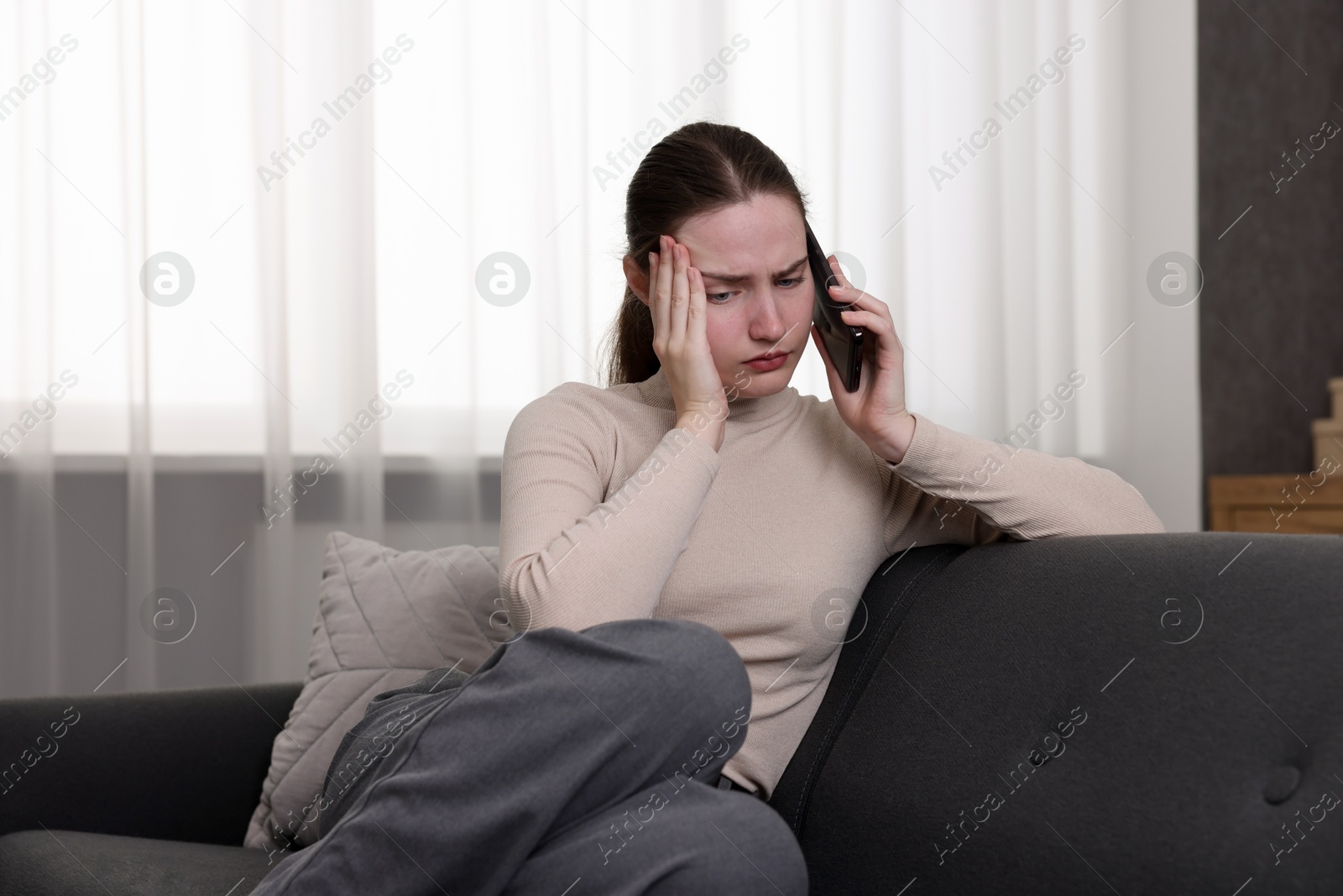 Photo of Depressed woman calling hotline for mental health help on sofa at home