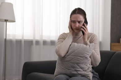 Photo of Depressed woman calling hotline for mental health help on sofa at home