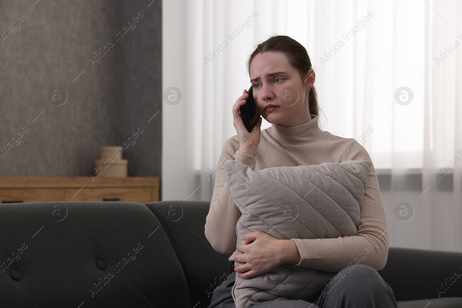 Photo of Depressed woman calling hotline for mental health help on sofa at home. Space for text