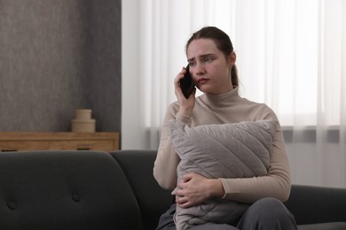 Photo of Depressed woman calling hotline for mental health help on sofa at home. Space for text