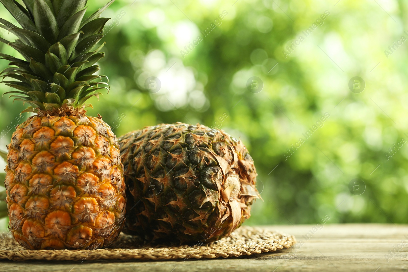 Photo of Fresh ripe pineapples on wooden table against blurred background, space for text