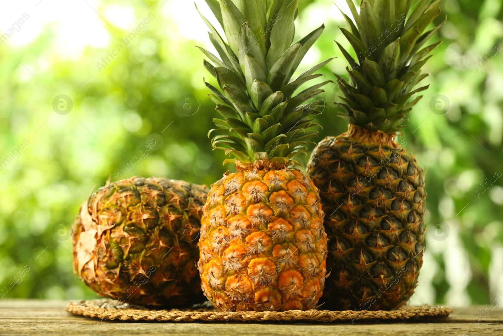 Photo of Fresh ripe pineapples on wooden table against blurred background