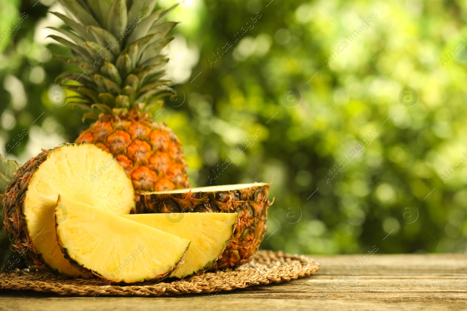 Photo of Fresh ripe pineapples on wooden table against blurred background, space for text