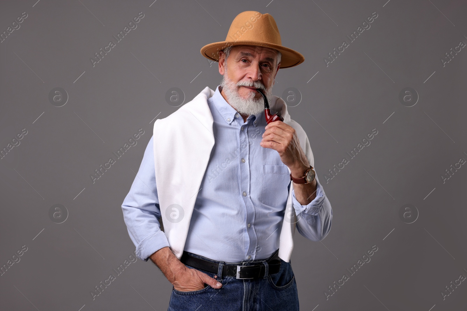 Photo of Bearded senior man with stylish hat and tobacco pipe on grey background