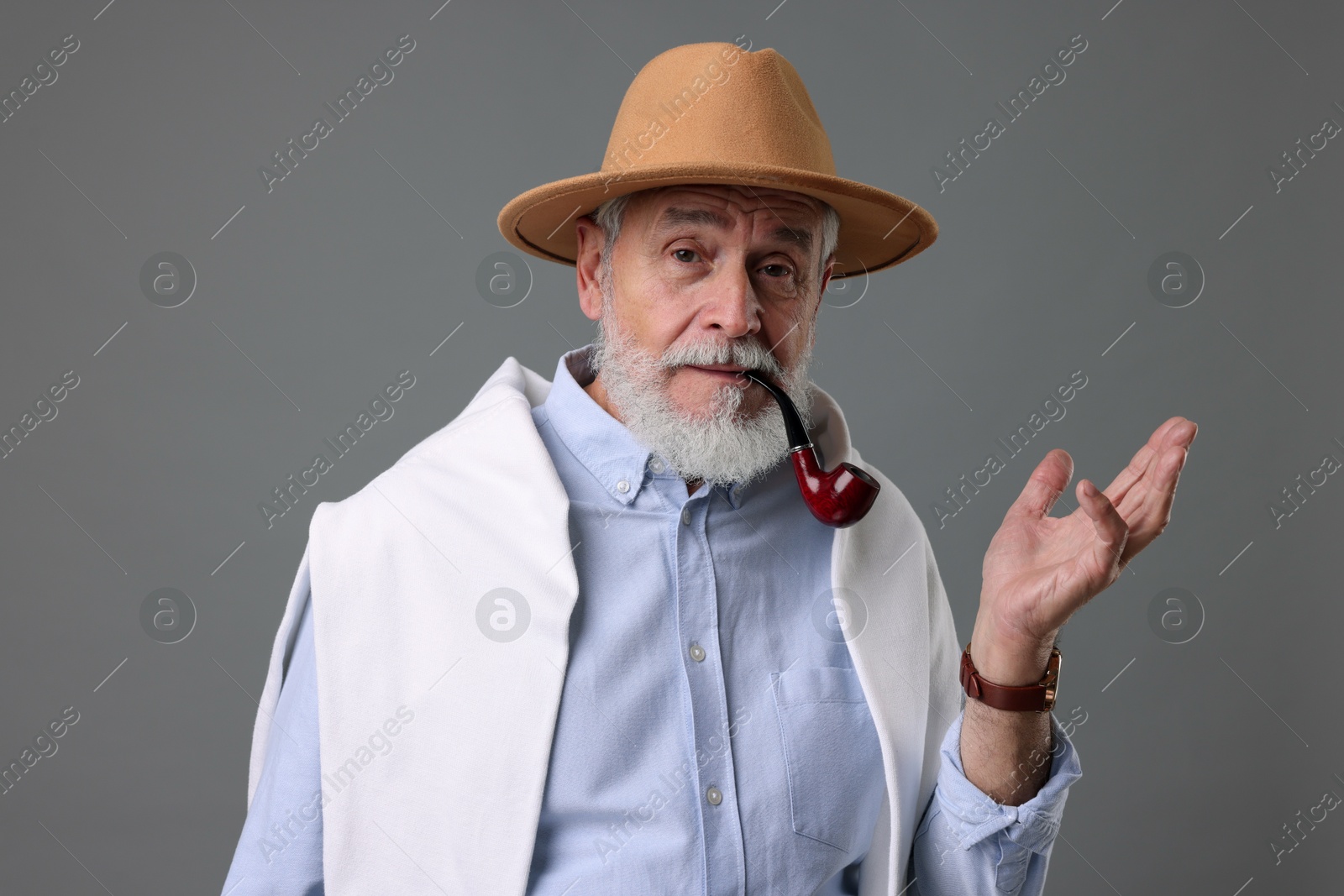 Photo of Bearded senior man with stylish hat and tobacco pipe on grey background