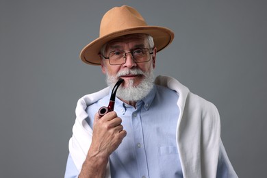 Photo of Bearded senior man with stylish hat and tobacco pipe on grey background