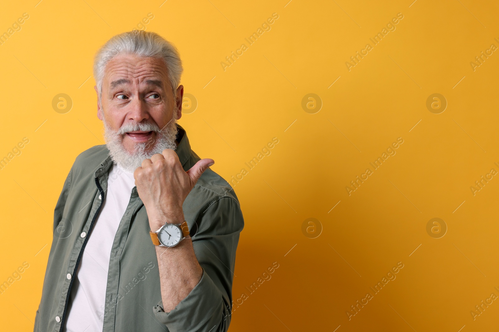 Photo of Senior man pointing at something on orange background. Space for text