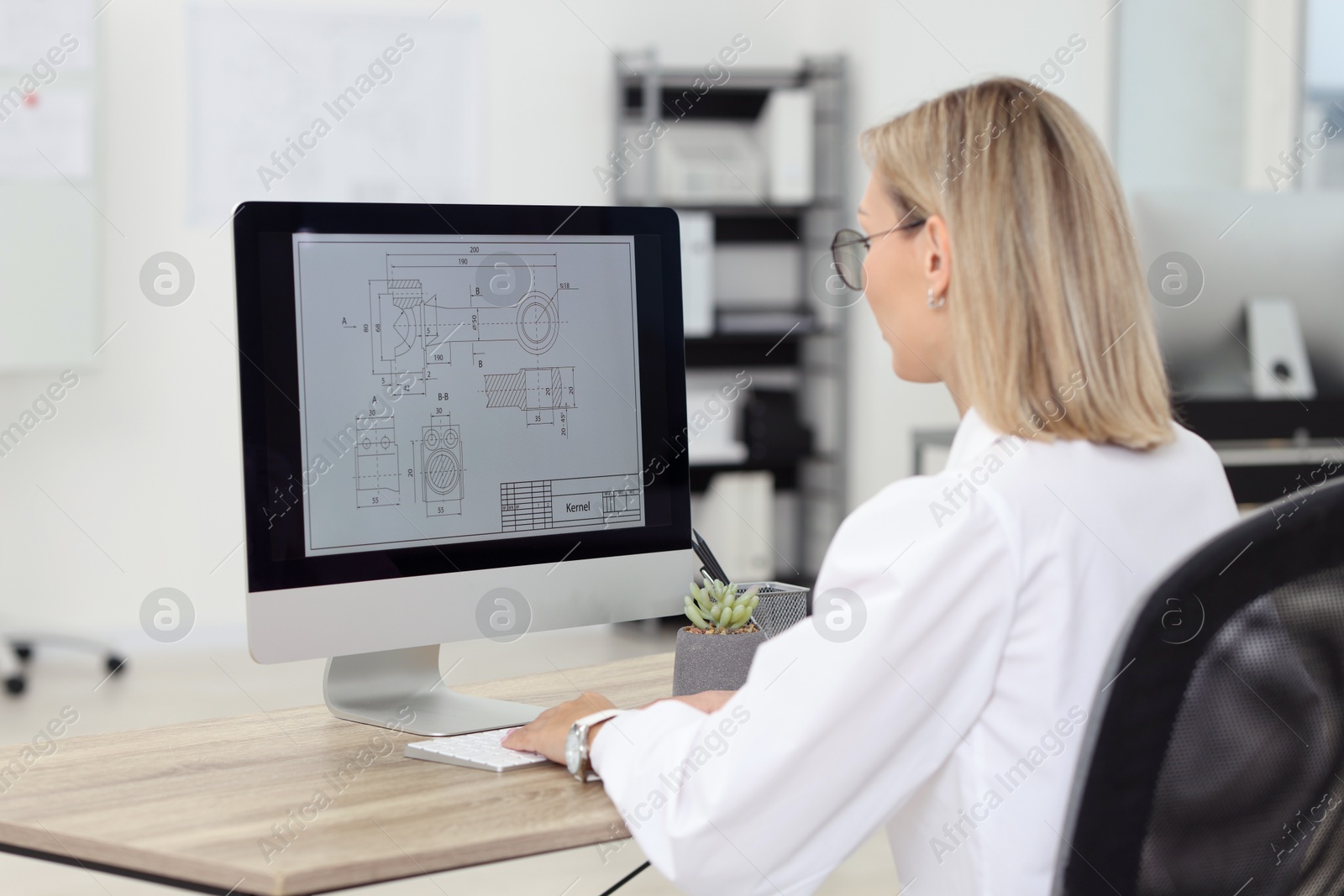 Photo of Technician making digital engineering drawing on computer at desk in office, back view