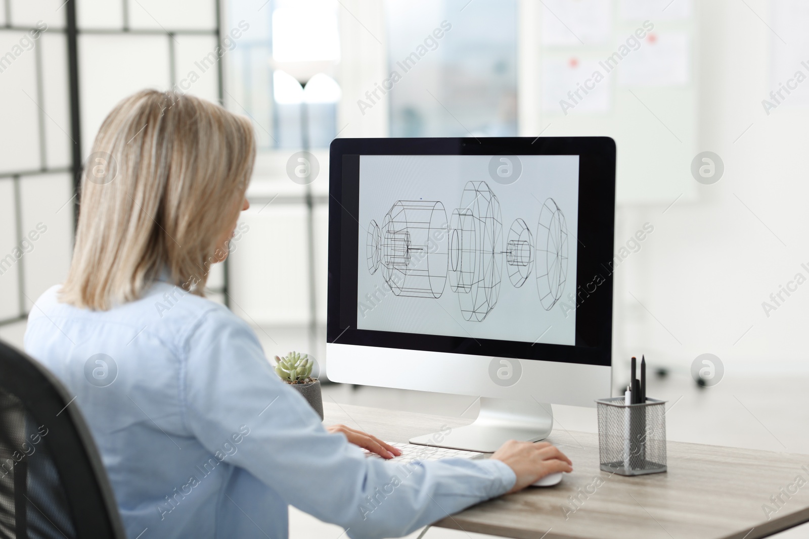 Photo of Technician making digital engineering drawing on computer at desk in office, back view