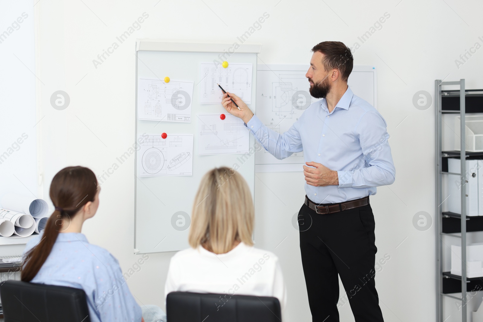 Photo of Man making presentation with engineering drawings to his colleagues in office