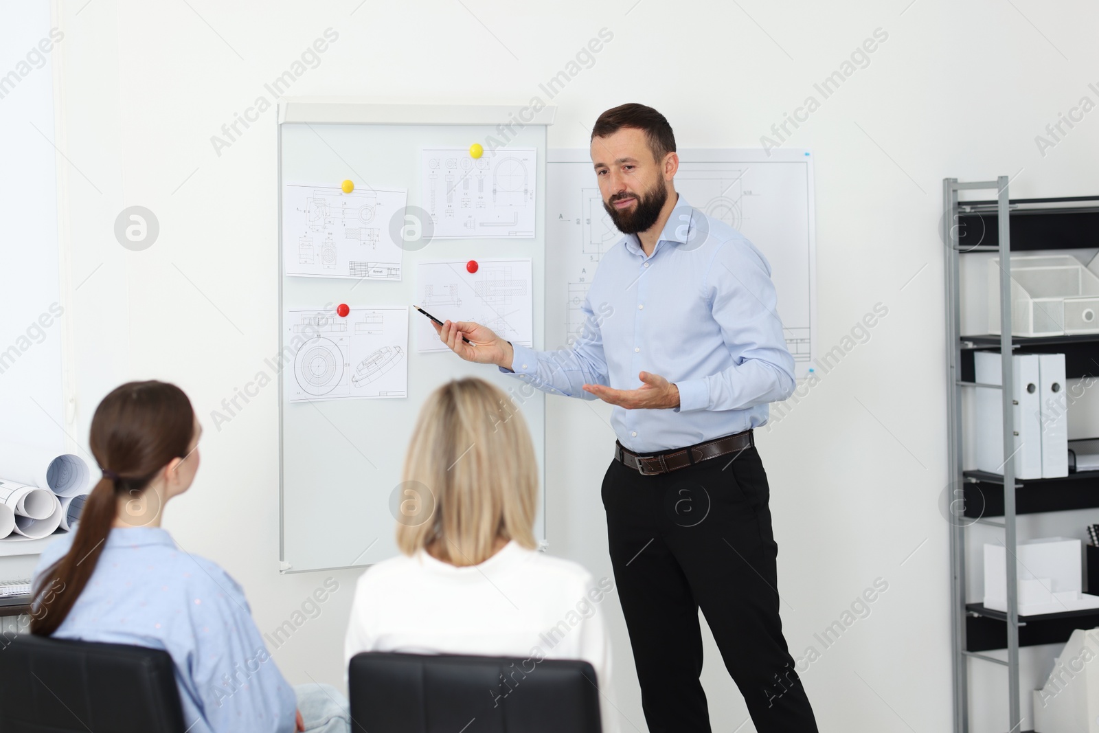 Photo of Man making presentation with engineering drawings to his colleagues in office