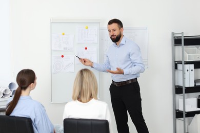 Photo of Man making presentation with engineering drawings to his colleagues in office