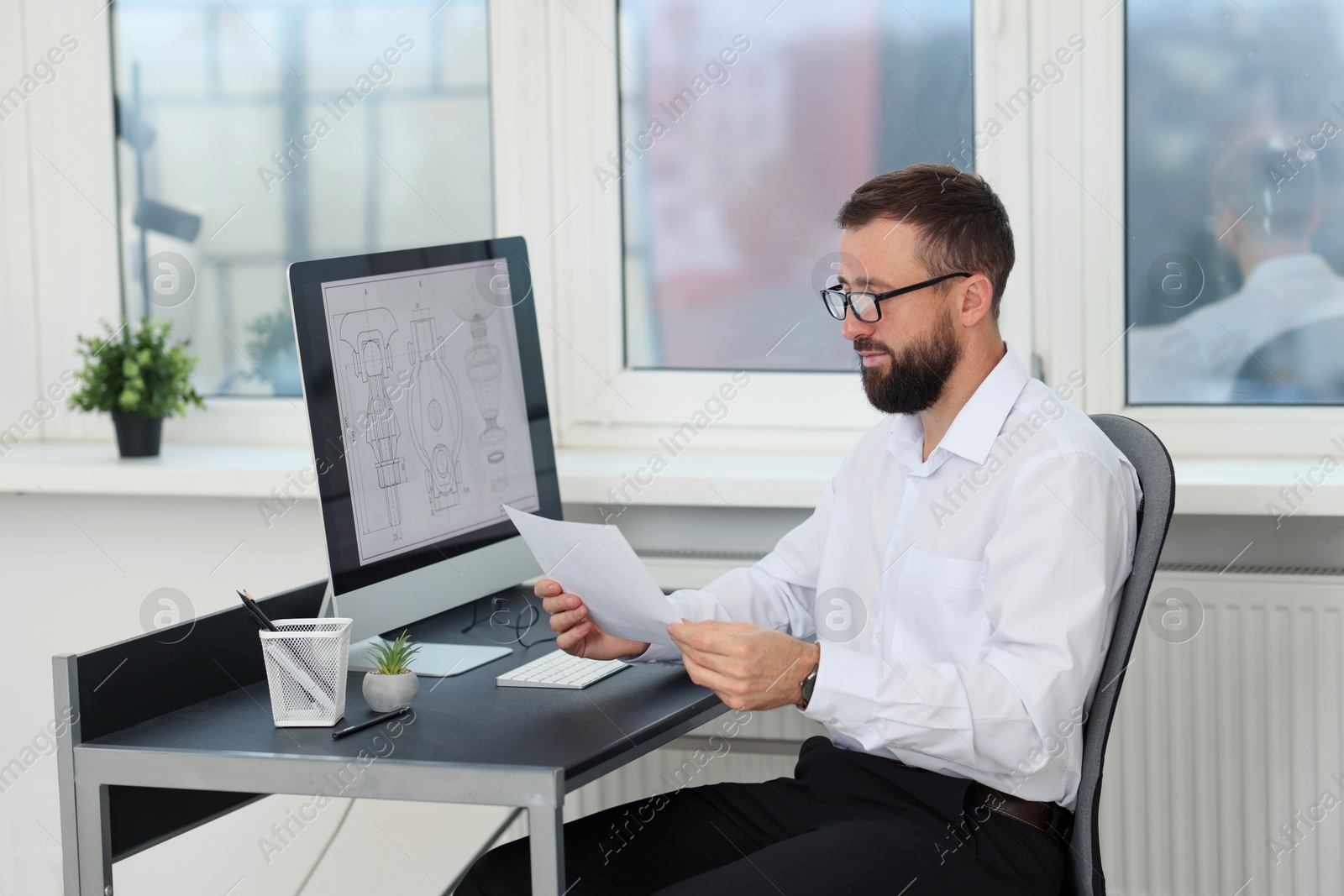 Photo of Technician making digital engineering drawing on computer at desk in office