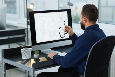 Photo of Technician making digital engineering drawing on computer at desk in office, back view