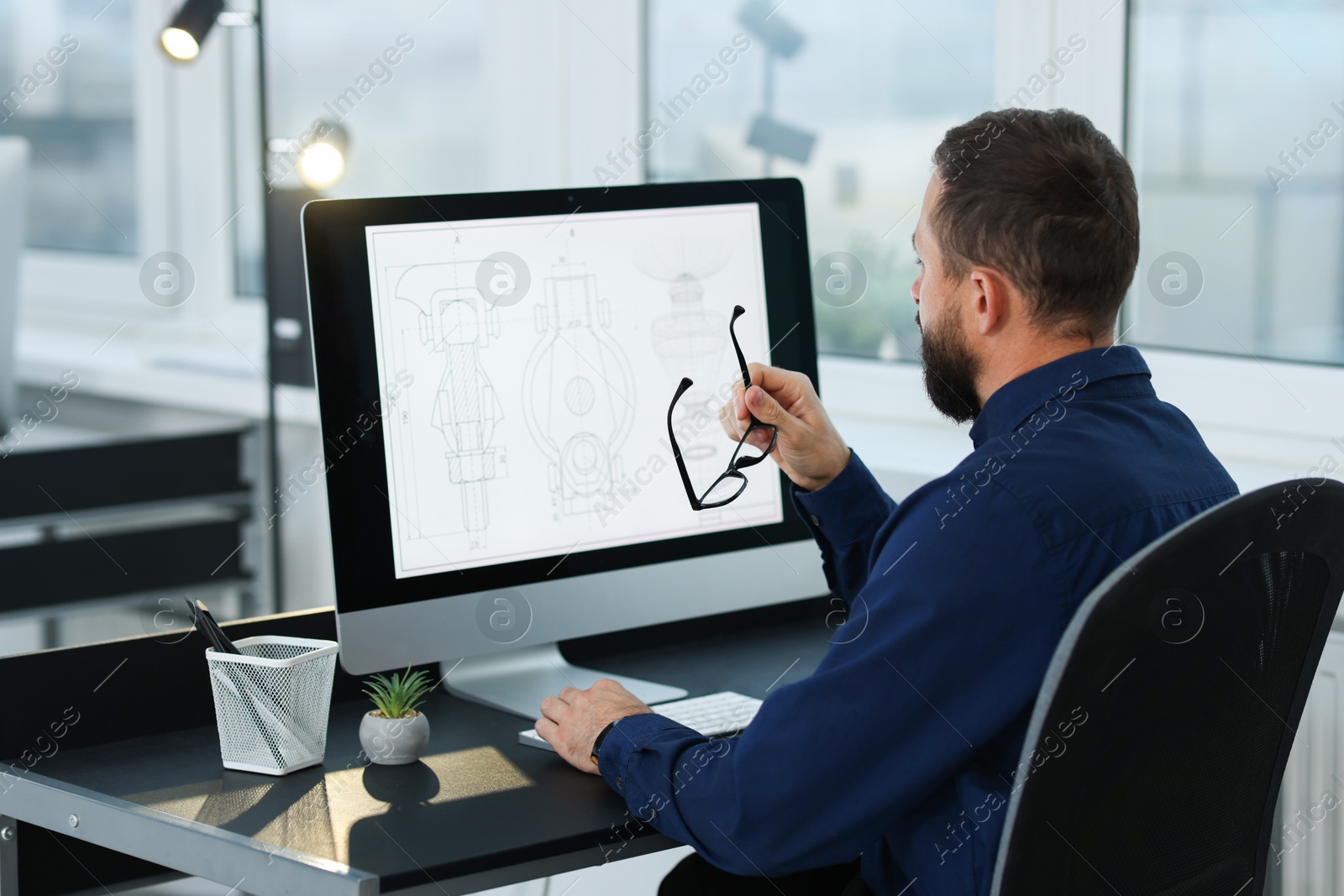 Photo of Technician making digital engineering drawing on computer at desk in office, back view