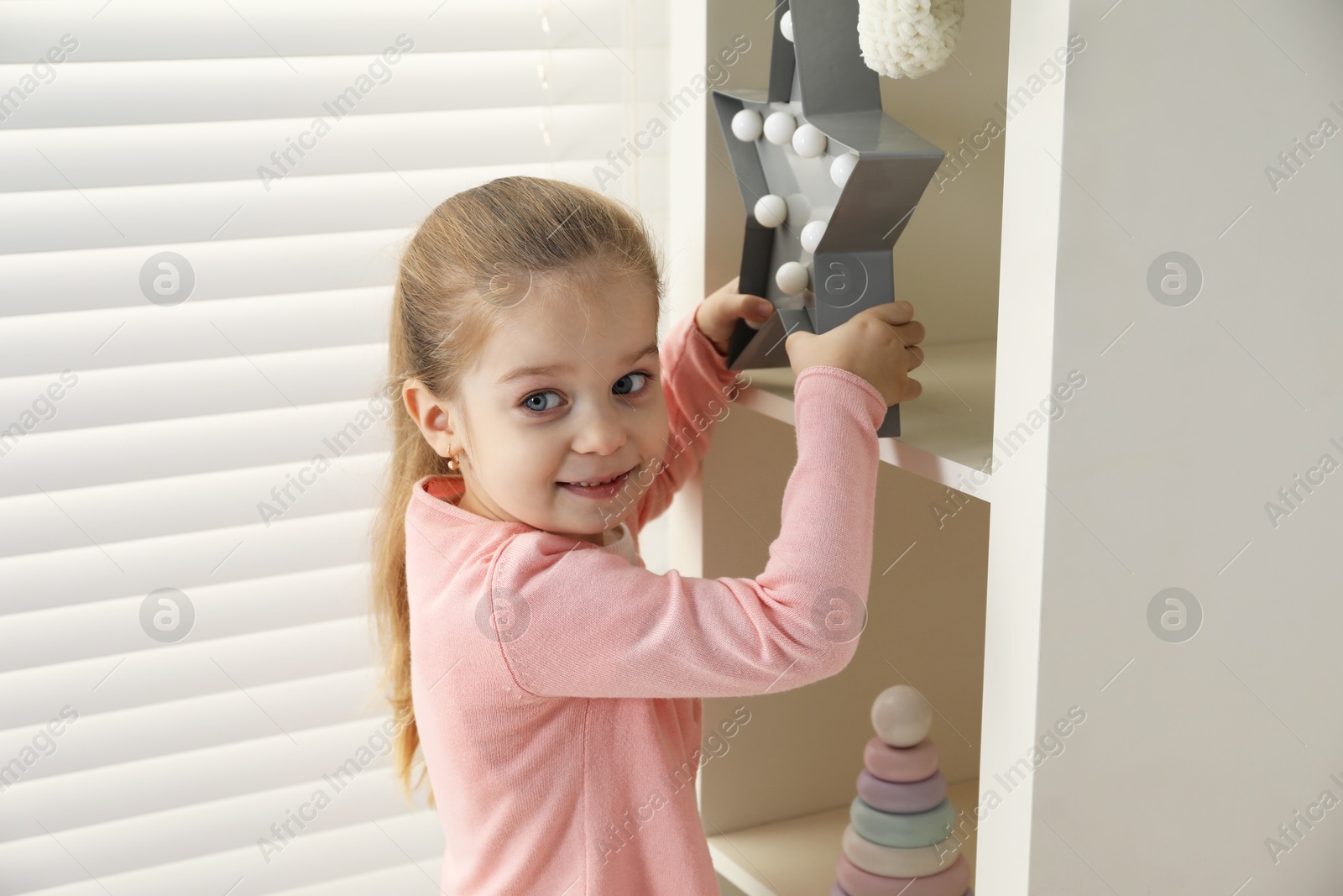 Photo of Little girl holding star decor near shelf at home