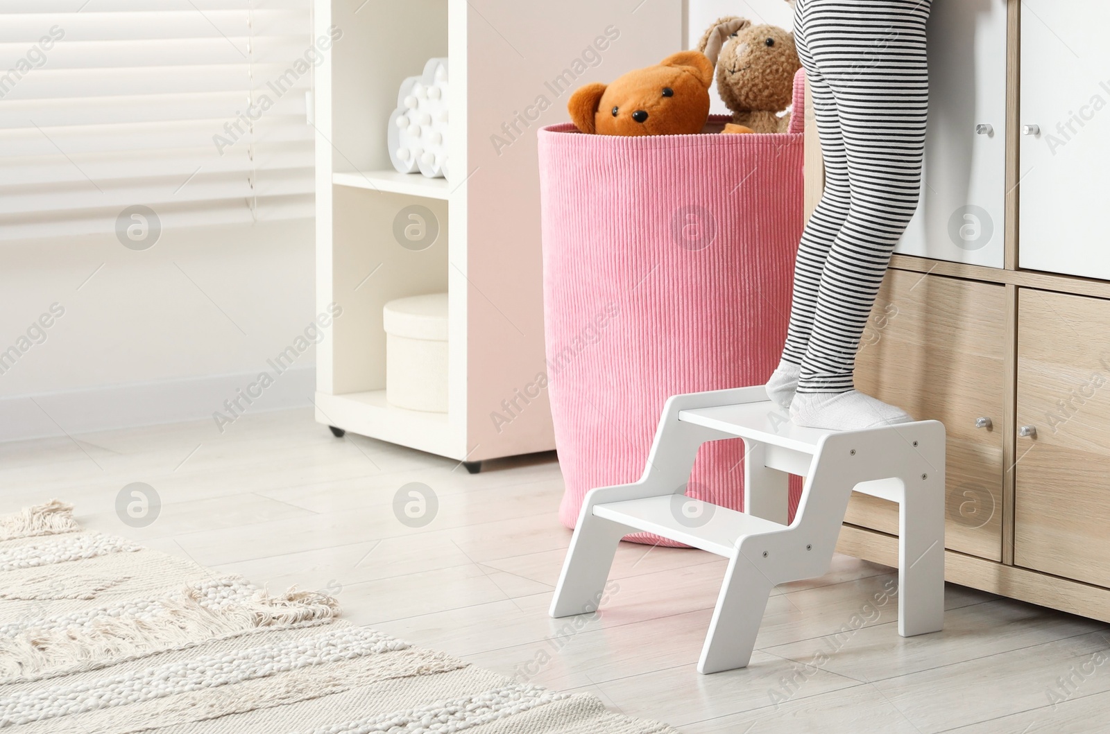 Photo of Little girl standing on step stool indoors, closeup. Space for text