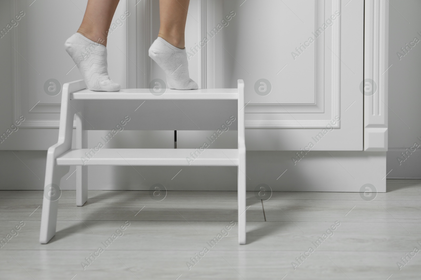 Photo of Little girl standing on step stool indoors, closeup