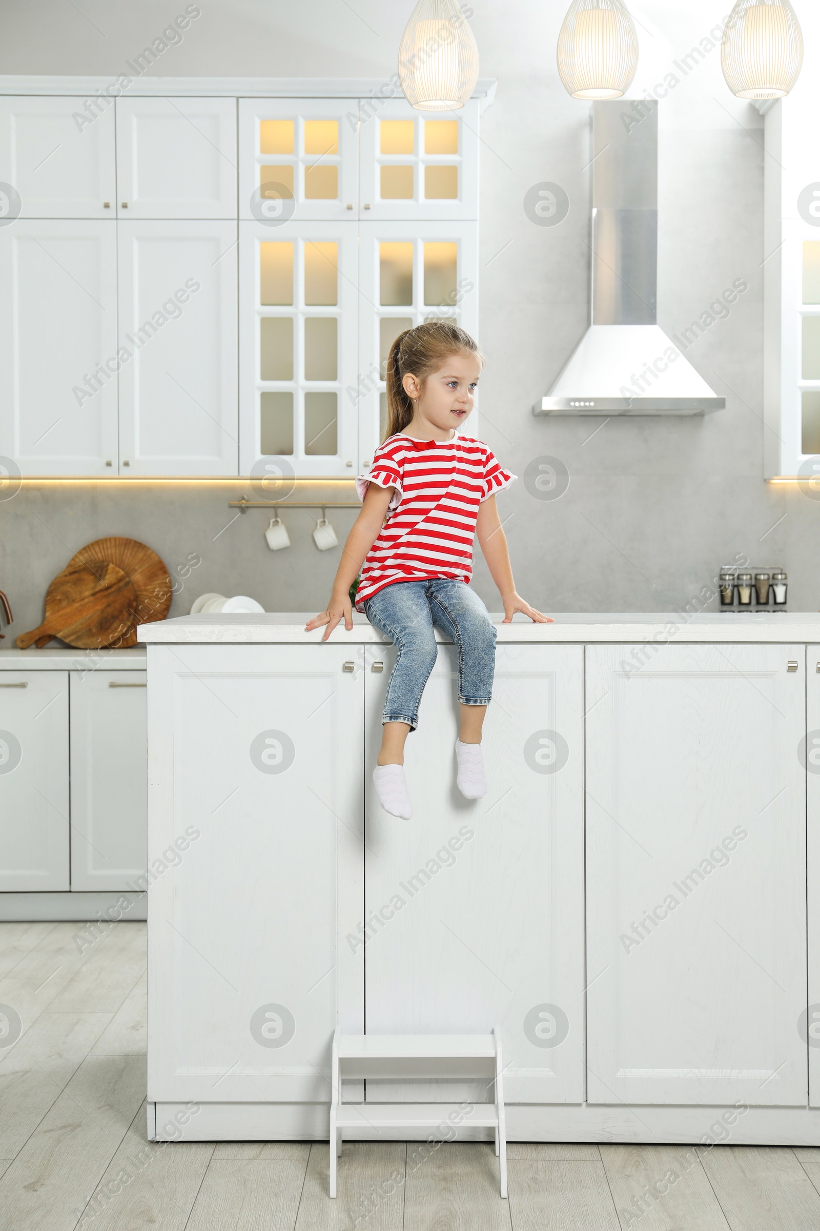 Photo of Little girl sitting on counter near step stool in kitchen