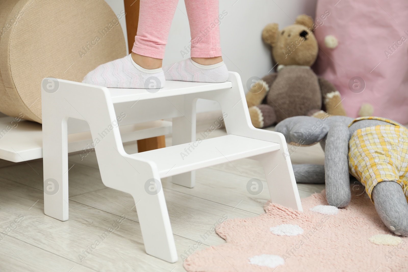 Photo of Little girl standing on step stool indoors, closeup