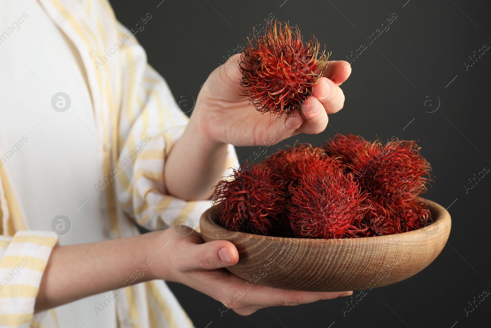 Photo of Woman holding fresh rambutans in bowl on black background, closeup