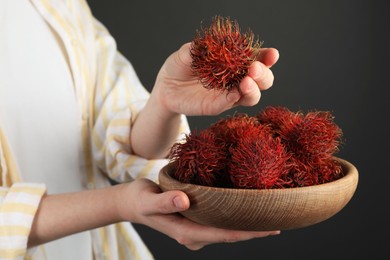 Photo of Woman holding fresh rambutans in bowl on black background, closeup