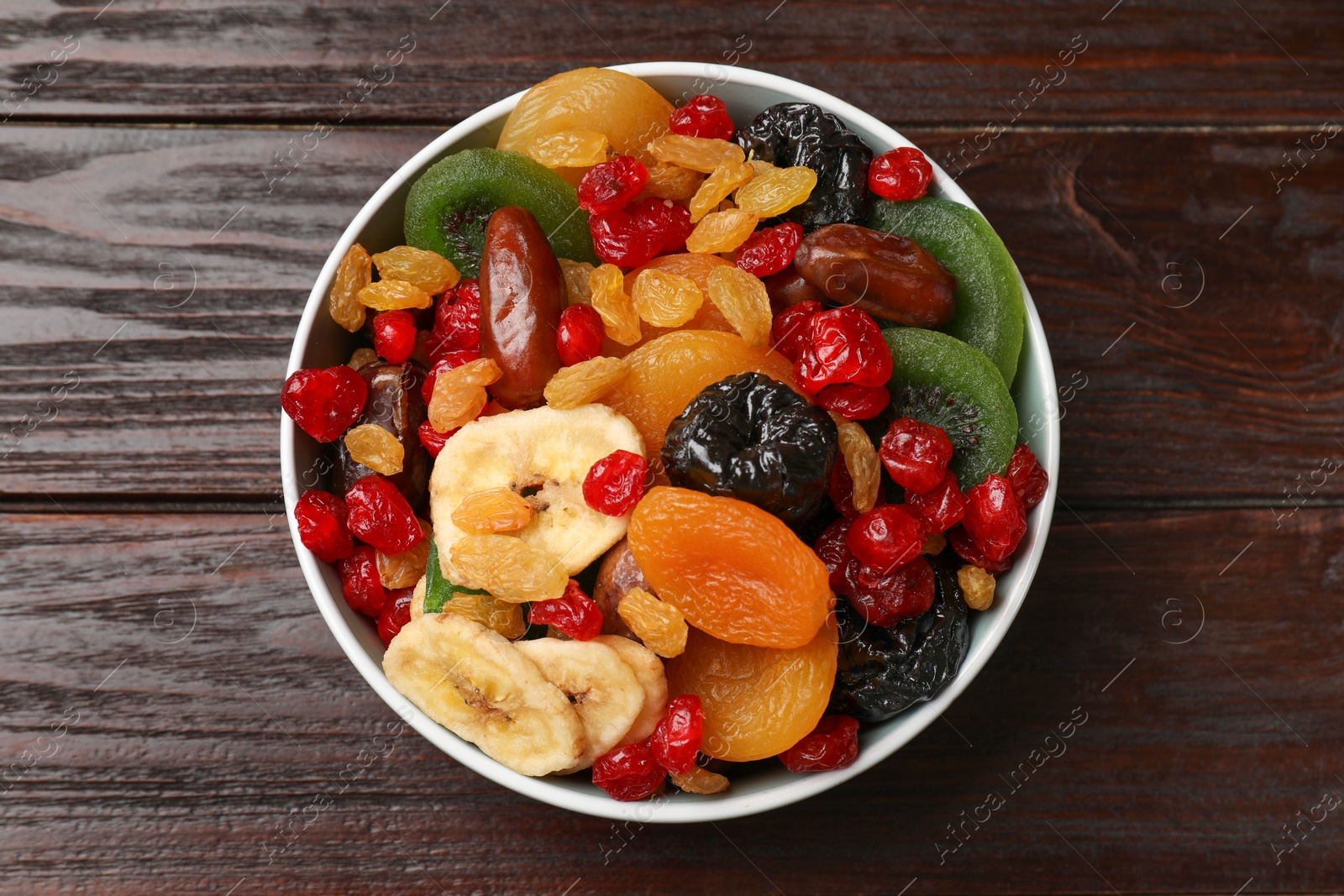 Photo of Mix of different dried fruits in bowl on wooden table, top view