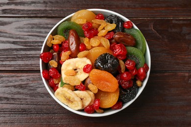 Photo of Mix of different dried fruits in bowl on wooden table, top view