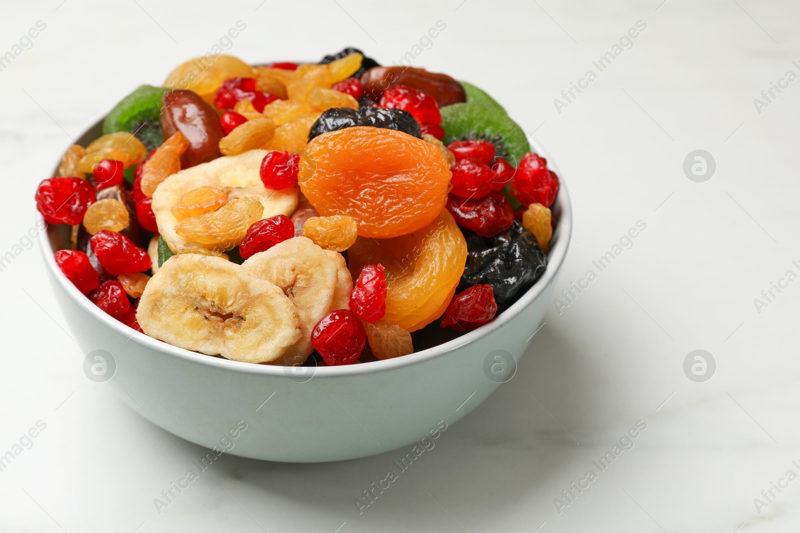 Photo of Mix of different dried fruits in bowl on white marble table, closeup