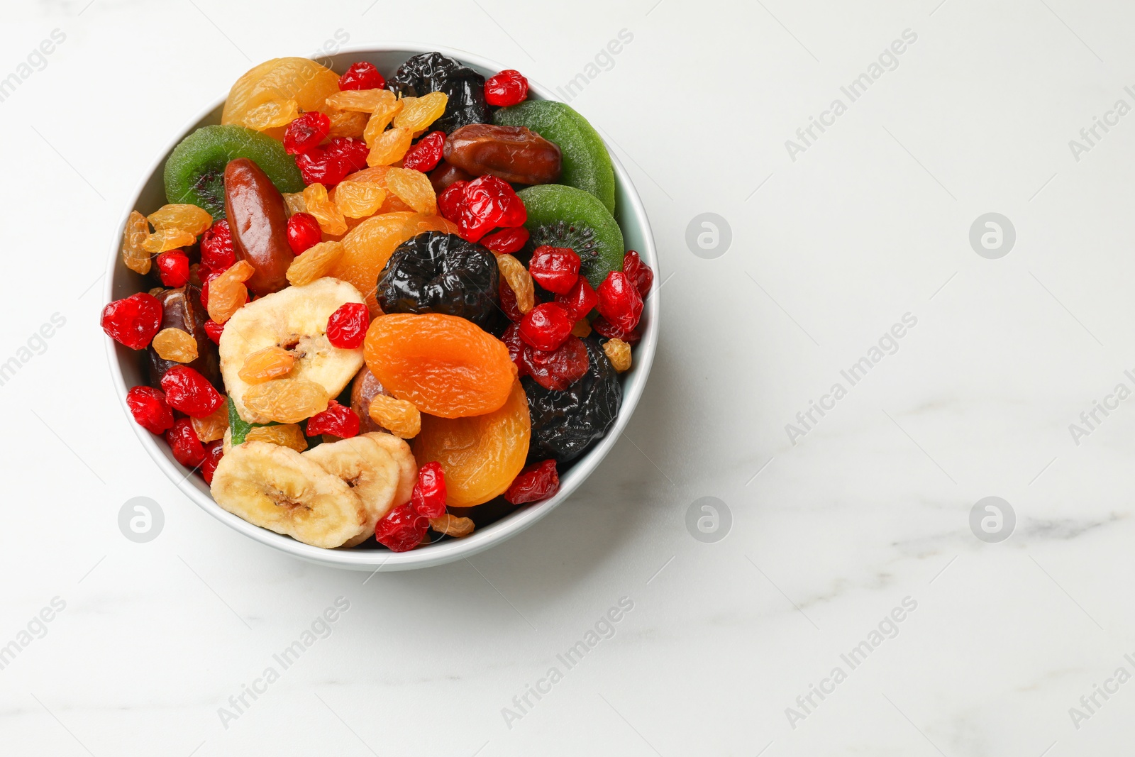 Photo of Mix of different dried fruits in bowl on white marble table, top view. Space for text