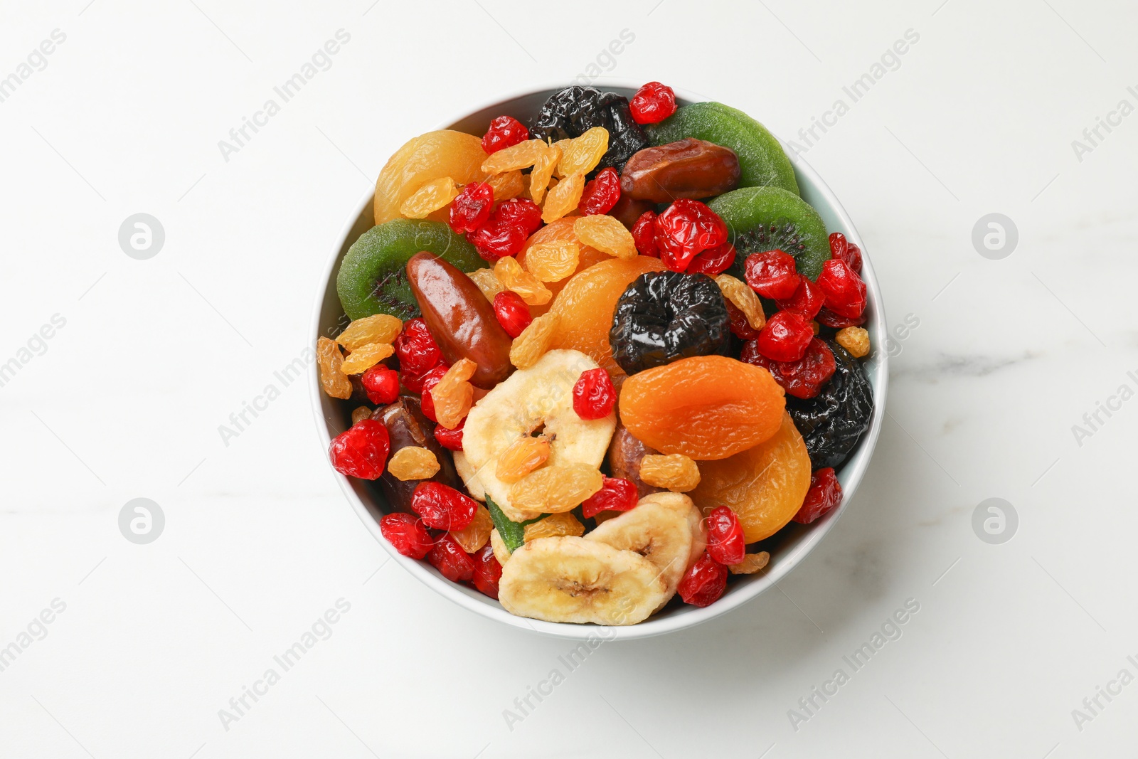 Photo of Mix of different dried fruits in bowl on white marble table, top view