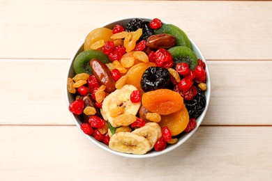 Photo of Mix of different dried fruits in bowl on wooden table, top view