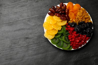 Photo of Mix of different dried fruits on black textured table, top view. Space for text