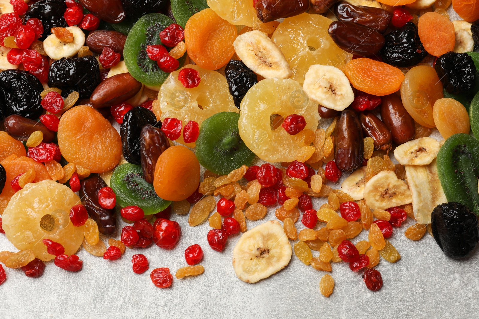 Photo of Mix of different dried fruits on gray textured table, top view