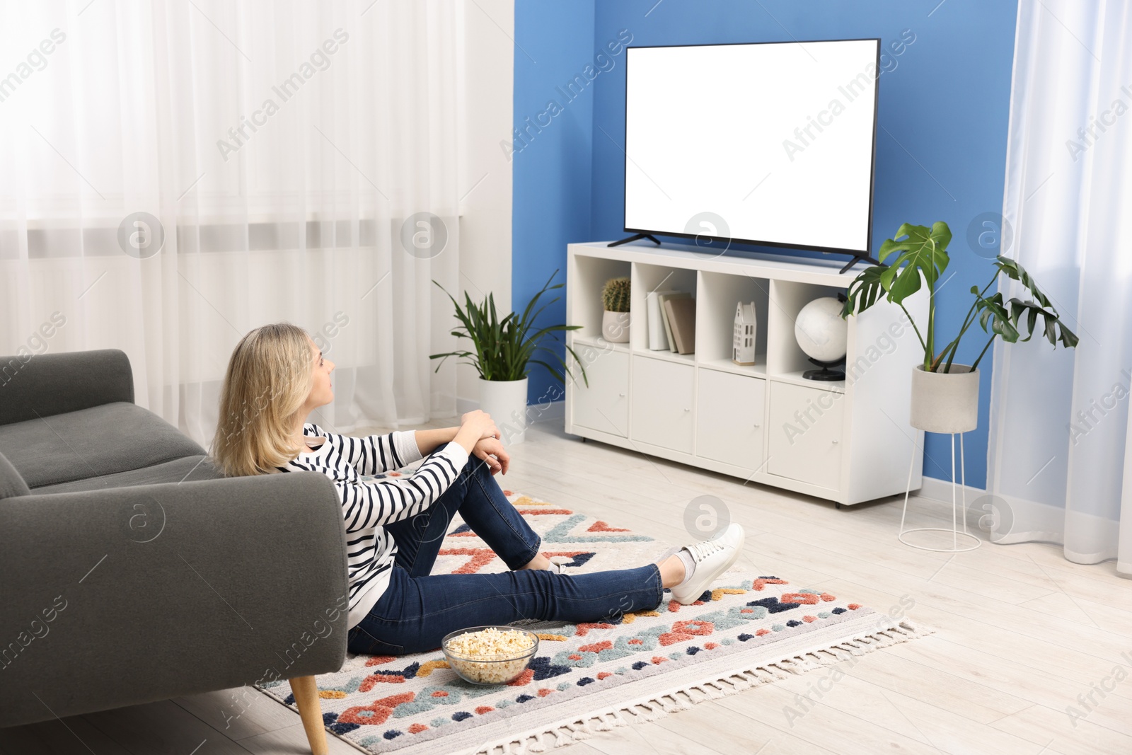 Photo of Woman with popcorn watching tv on floor at home