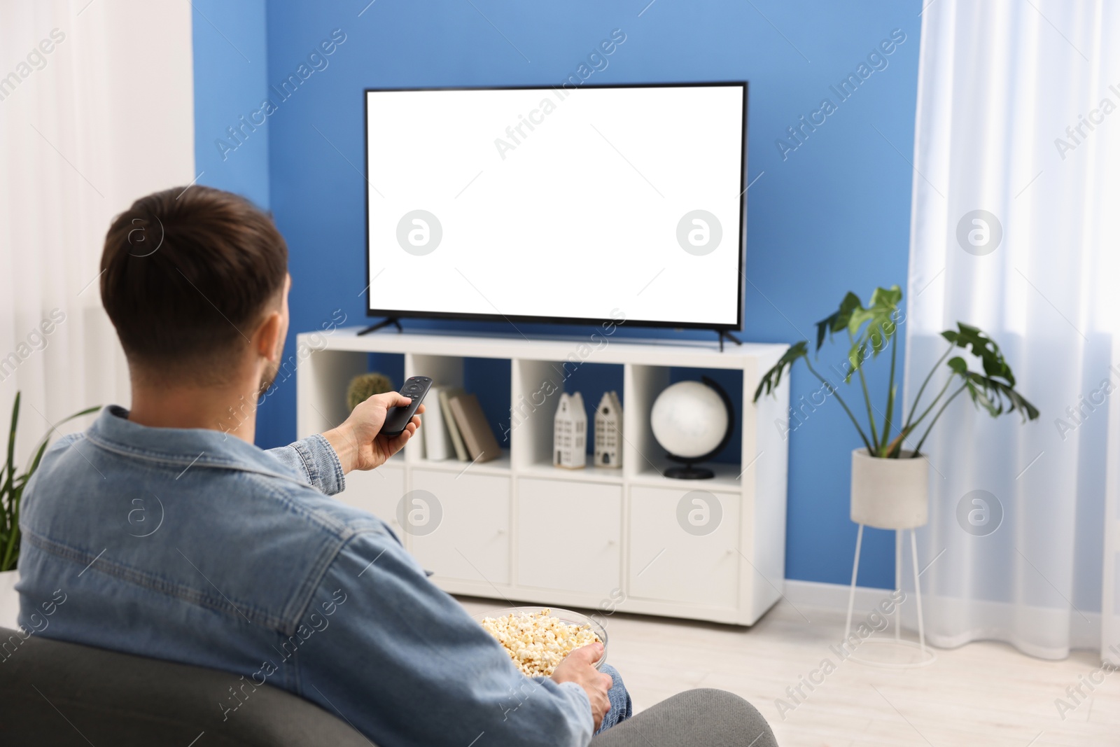 Photo of Man with popcorn watching tv on couch at home, back view