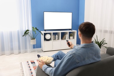 Photo of Man with popcorn watching tv on couch at home, back view