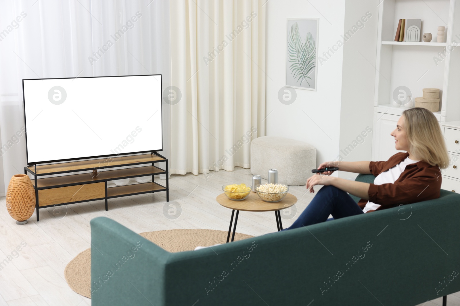 Photo of Woman with snacks and drinks watching tv on couch at home