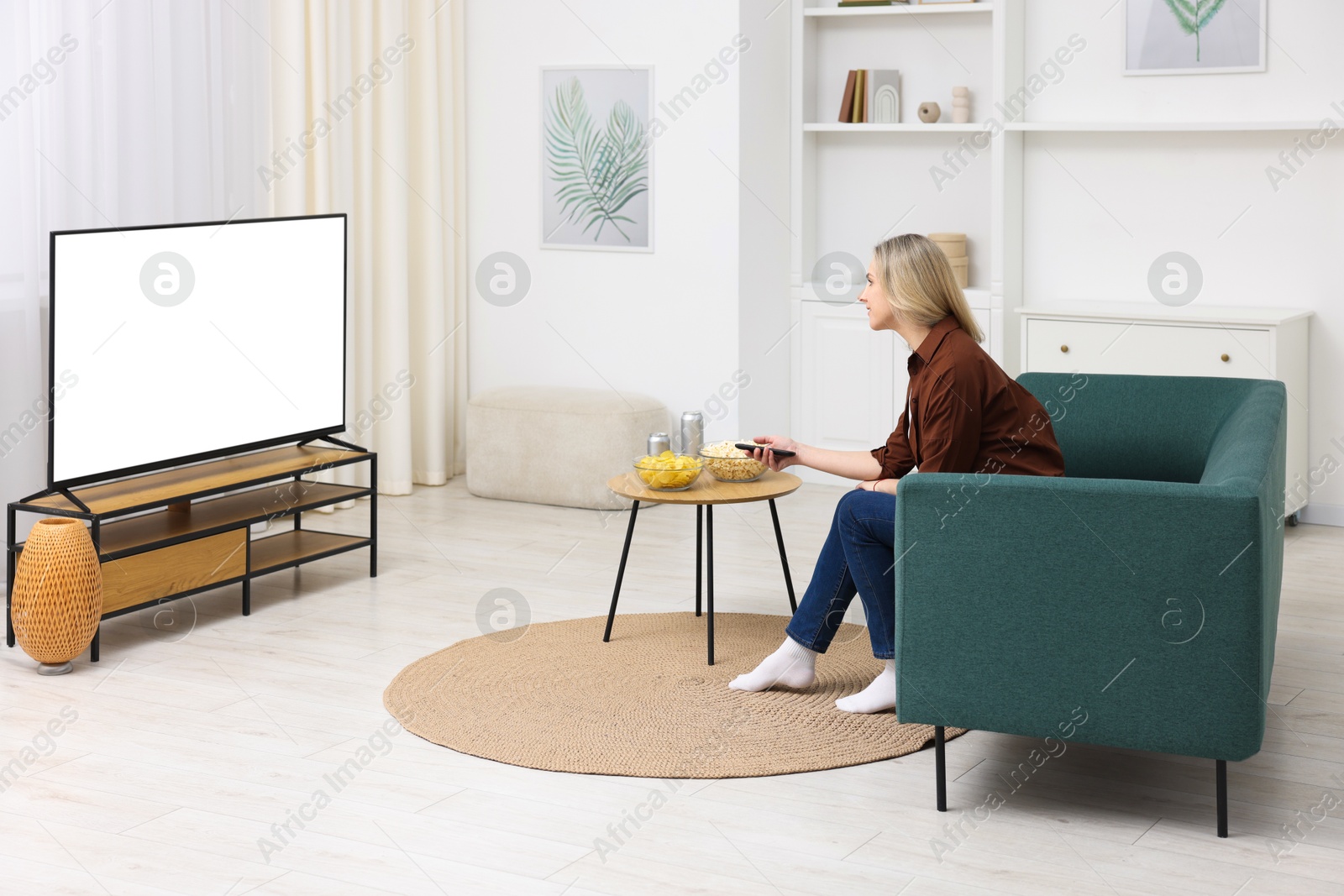 Photo of Woman with snacks and drinks watching tv on couch at home