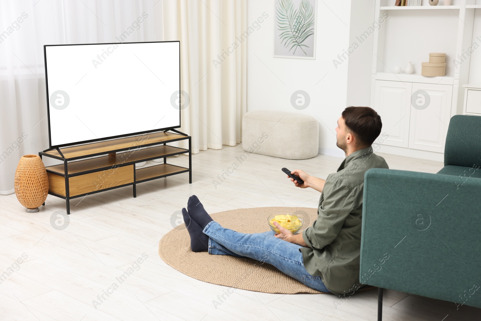 Photo of Man with chips watching tv on floor at home