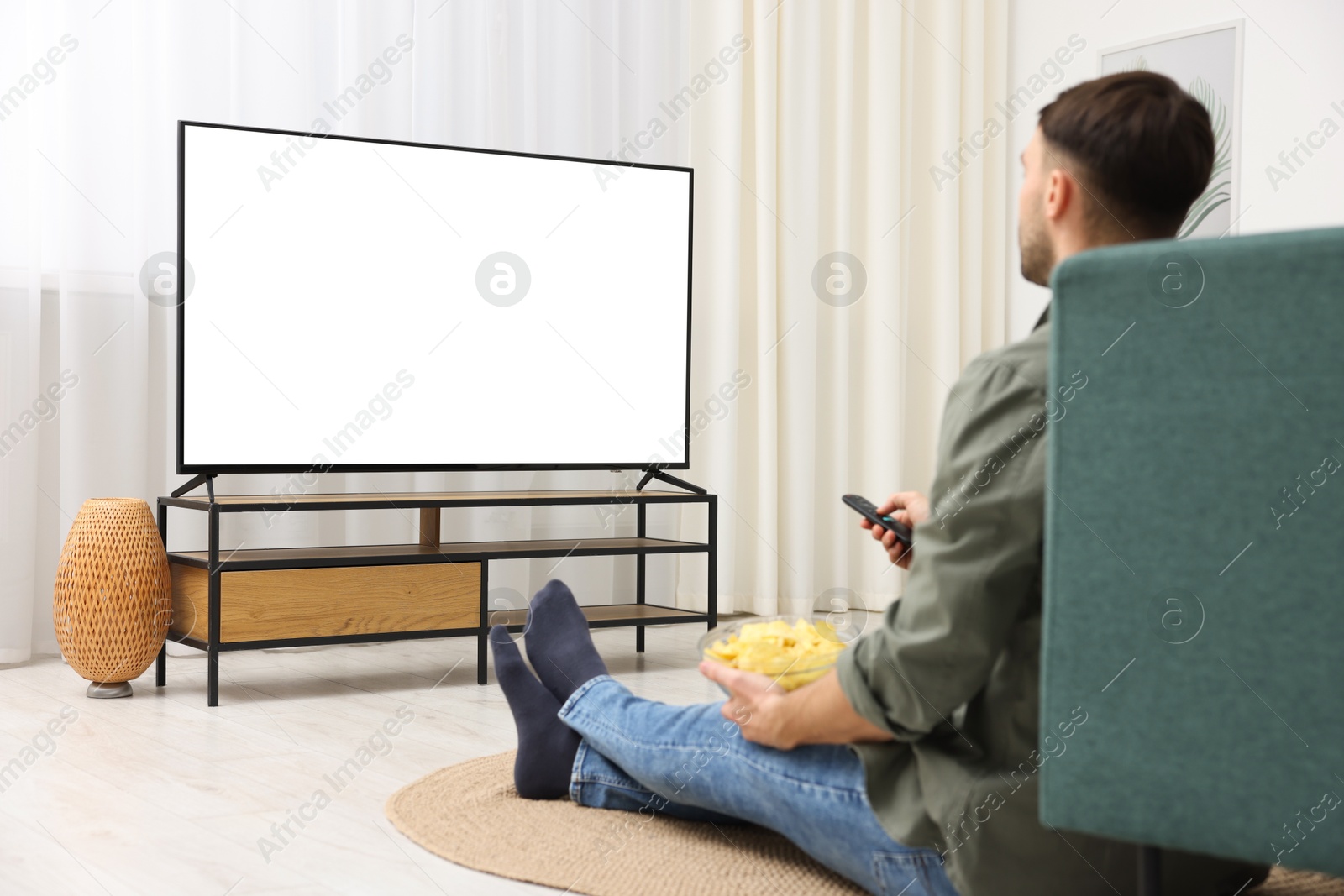 Photo of Man with chips watching tv on floor at home