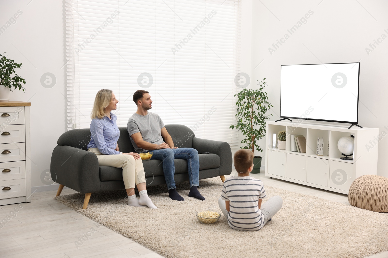 Photo of Happy family with snacks watching tv together at home